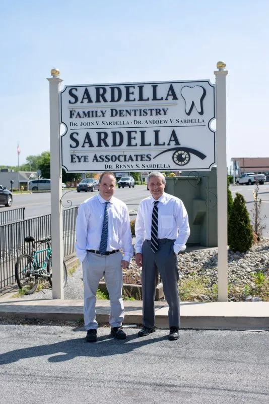 Two dentists standing in front of Sardella Family Dentistry sign — professional portrait